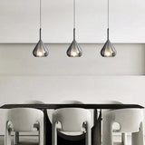 Three teardrop shades in a row above a dining table and pale chairs