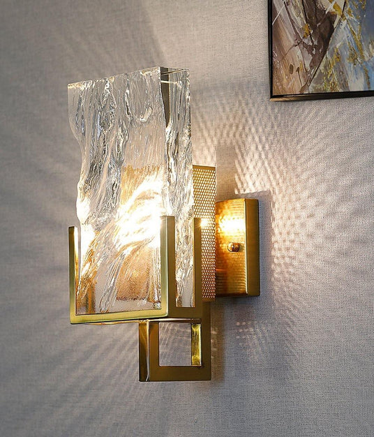 The sconce lit on a textured wall beside a framed abstract painting