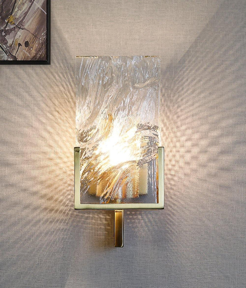 The sconce lit below the corner of a framed artwork, patterns of light on the wall