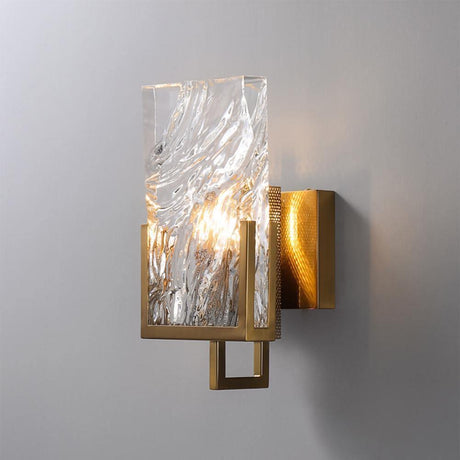 The sconce lit on a gray wall, light passing through the rippled glass