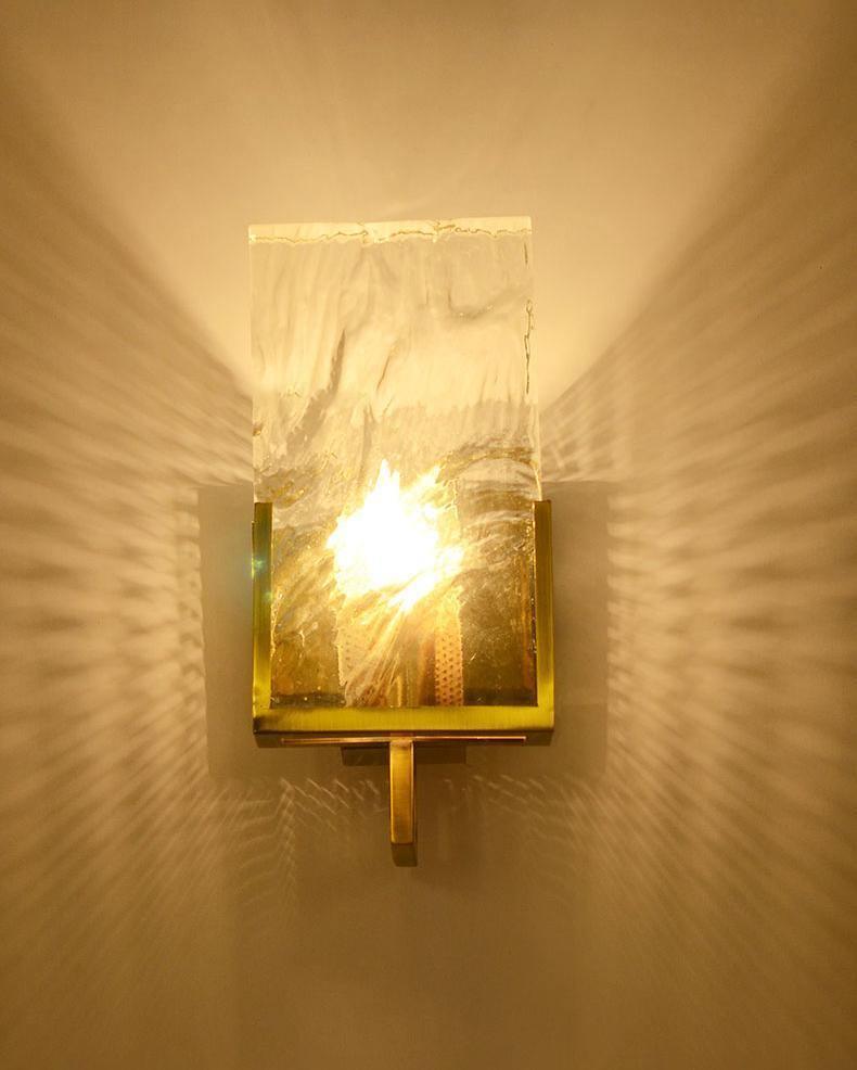 The sconce glowing on a warm wall, the frame outlined in brass