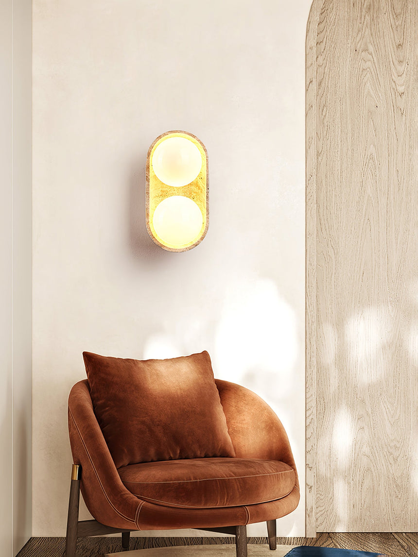 Sconce lit above a rust velvet armchair beside a wood panel and a cushion