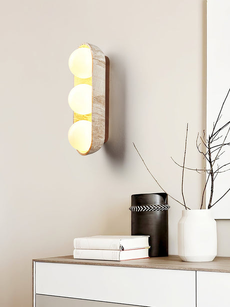 Sconce lit above a white dresser holding a vase of branches and two books