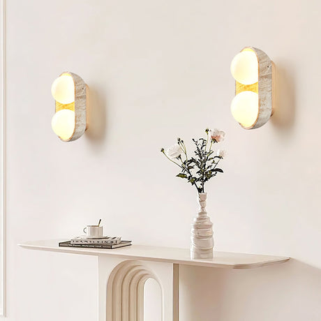 Two sconces lit on a wall above a fluted console holding a vase of flowers