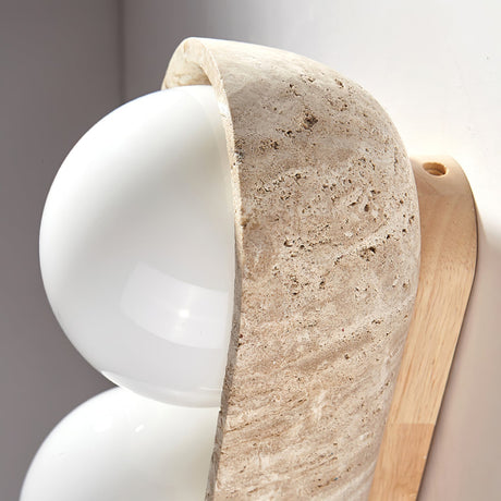 The carved travertine lip curving over the top of a white glass orb