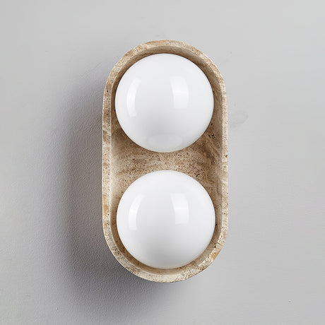 Two white glass orbs sitting unlit in the short stone shell on a gray ground