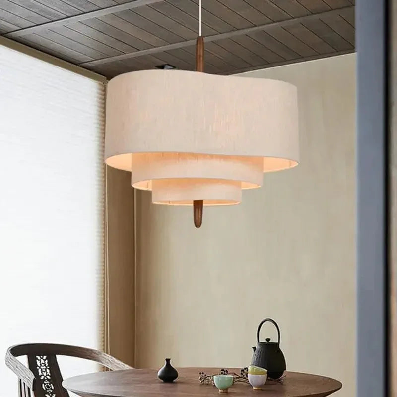 Two tier drum shade lit above a table beside a window