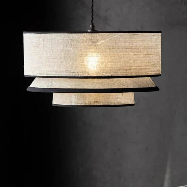 Tiered drum pendant light with three hand knitted bands lit against a dark wall