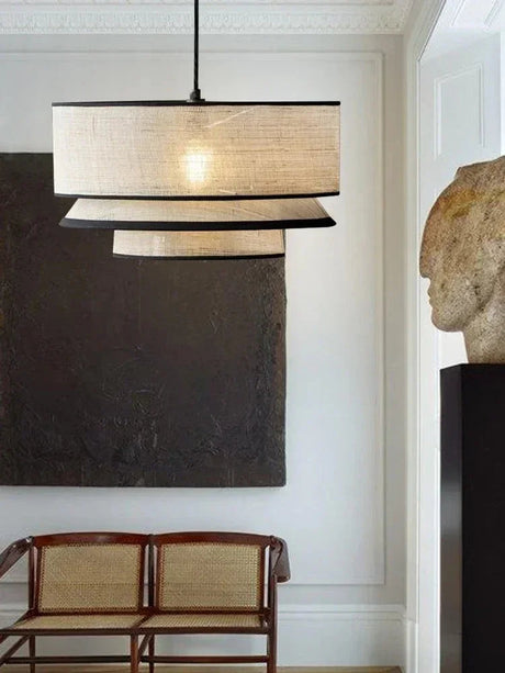 Tiered drum pendant light lit in a dark interior with dining chairs