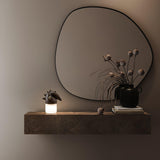 Touch control bedside lamp lit on a shelf below a round mirror