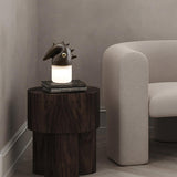 Touch control bedside lamp lit on a dark side table by a chair