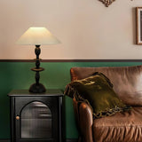 Spindle table lamp lit on a cabinet beside a brown leather sofa