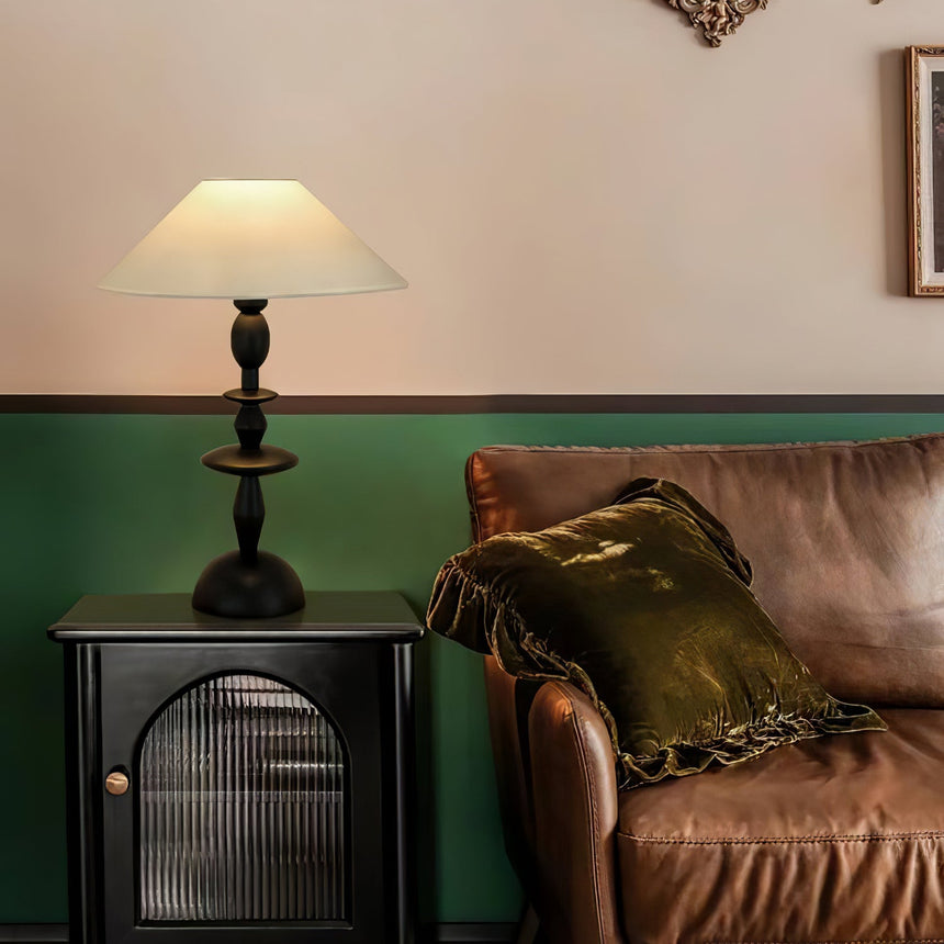 Spindle table lamp lit on a cabinet beside a brown leather sofa
