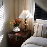 Spindle table lamp lit on a trunk beside a window with white blinds