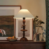 Spindle table lamp lit on a sideboard in front of two framed pictures