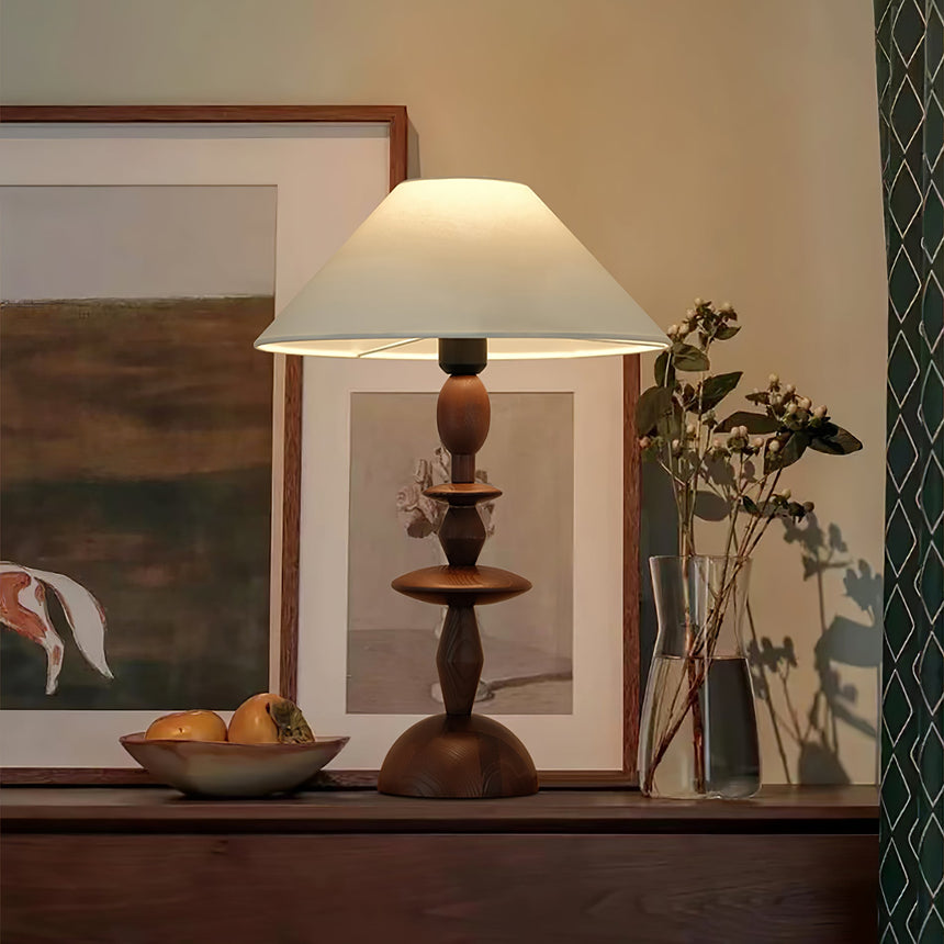 Spindle table lamp lit on a sideboard in front of two framed pictures
