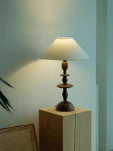 Spindle table lamp lit on a pale wood block against a green wall