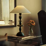 Spindle table lamp lit on a console beside a small vase of orange flowers