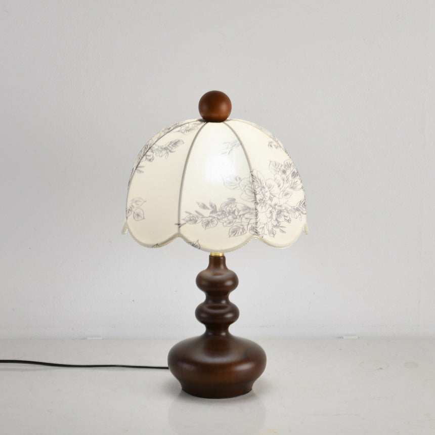 Toile shade lamp lit with a cooler bulb against a white wall