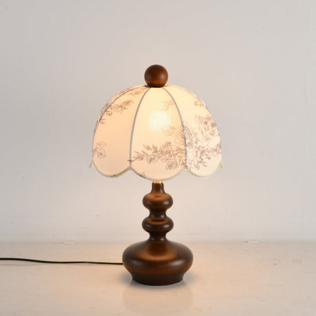 Toile shade lamp lit with a warm bulb, the scalloped hem in shadow