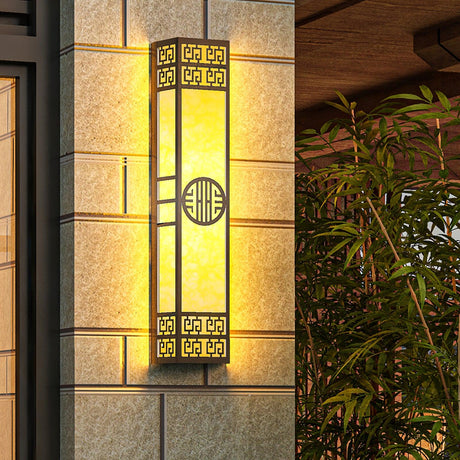 The light lit on a stone tile wall beside a doorway, bamboo leaves at the edge