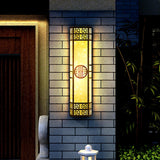 The column light glowing on a gray brick wall beside a wood front door and bamboo