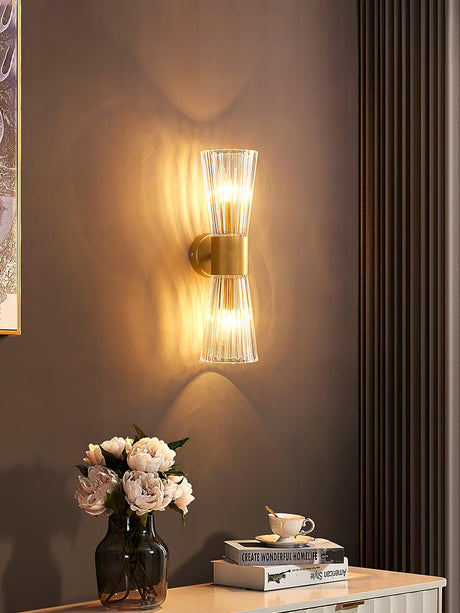 The sconce lit on a brown wall above a dresser with roses and books
