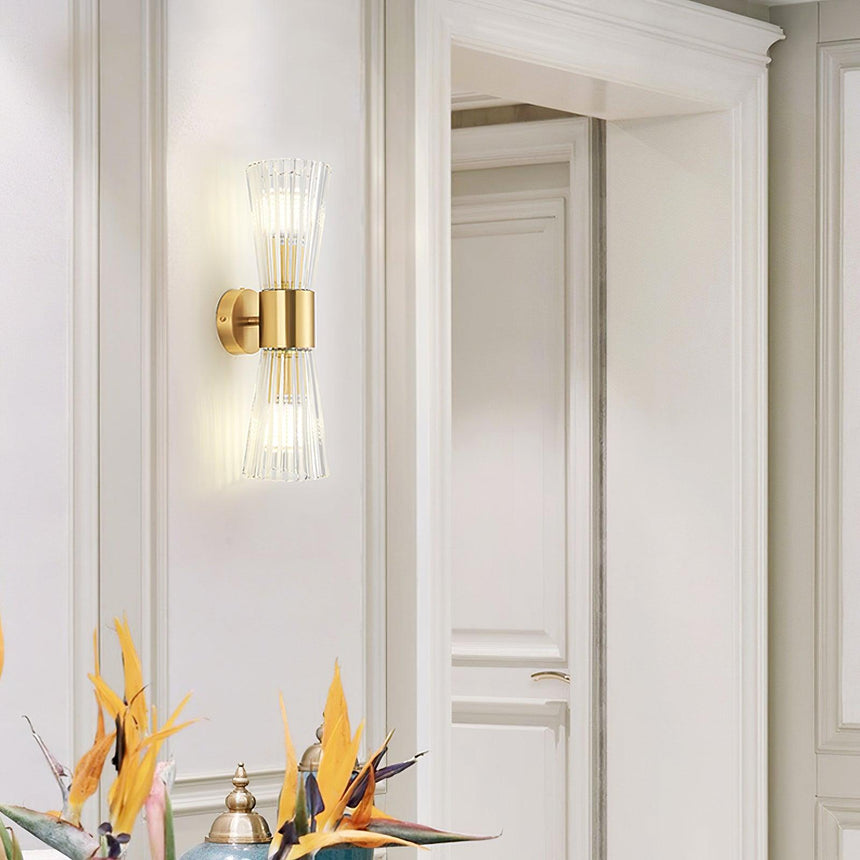The sconce lit on a white paneled wall above a vase of bird of paradise flowers