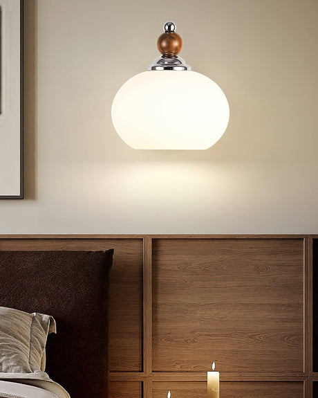 Sconce lit above a wood cabinet beside a bed with a candle burning