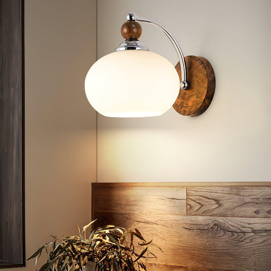 Sconce lit beside a wood headboard with olive branches in a vase below