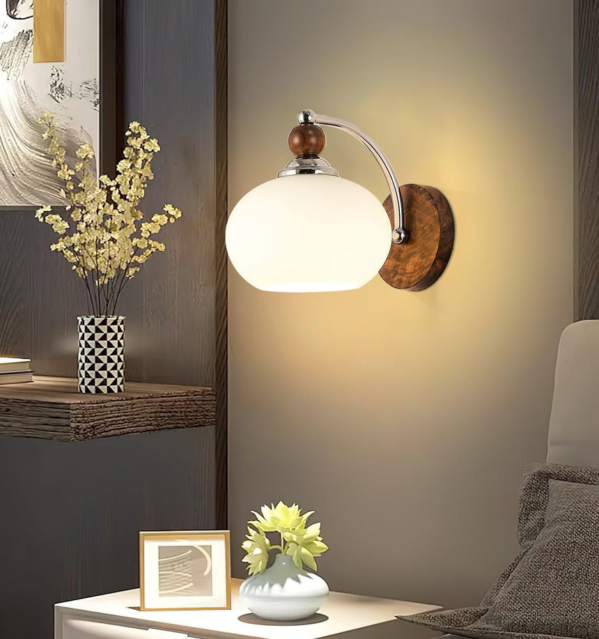 Sconce lit above a nightstand with a framed photo and a small plant
