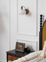 Sconce lit on a panel wall beside a spindle bed and a dark nightstand