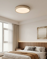 Round travertine ceiling light in a bedroom with a framed landscape and sheer curtains