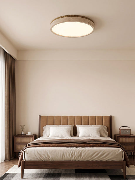 Round travertine ceiling light in a bedroom with a padded headboard and brown curtains