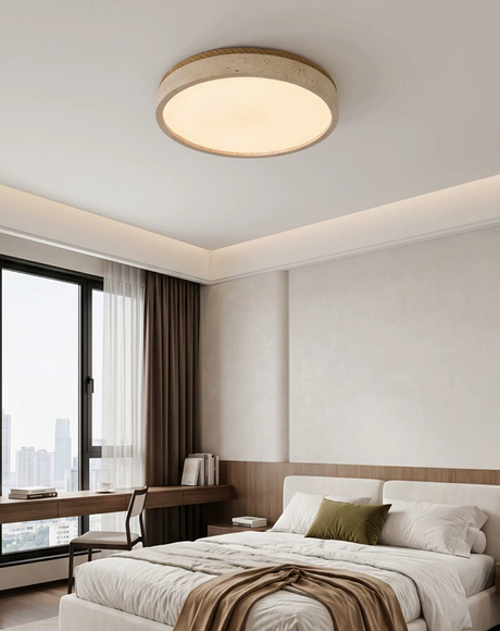 Round travertine ceiling light lit in a bedroom with a low wood headboard