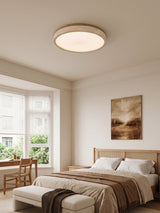 Round travertine ceiling light above a bed beside a window with a garden view