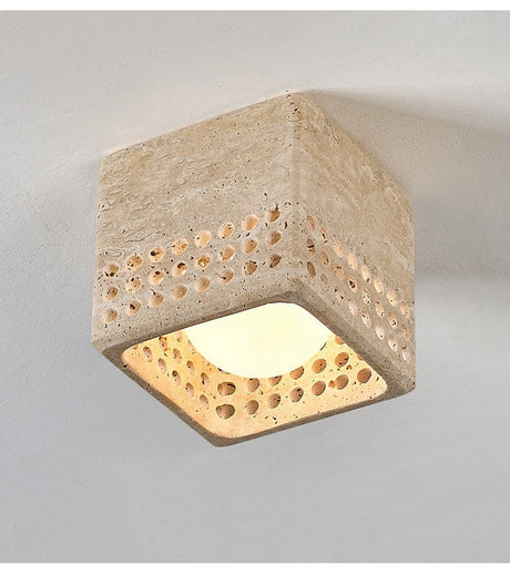 Square travertine block ceiling light lit, showing light through the drilled holes