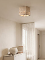Square travertine block ceiling light above a plaster console and a round vase