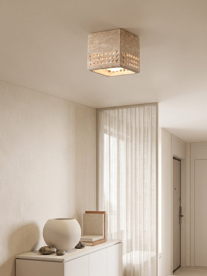 Square travertine block ceiling light above a plaster console and a round vase