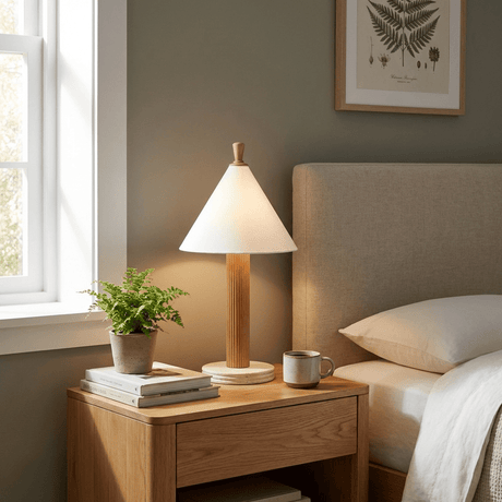 Travertine table lamp lit on a wood nightstand beside a bed