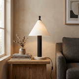 Travertine table lamp lit on a wood side table beside a sofa