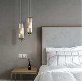 Two tube pendants hung beside a bed with a wooden headboard and shelf