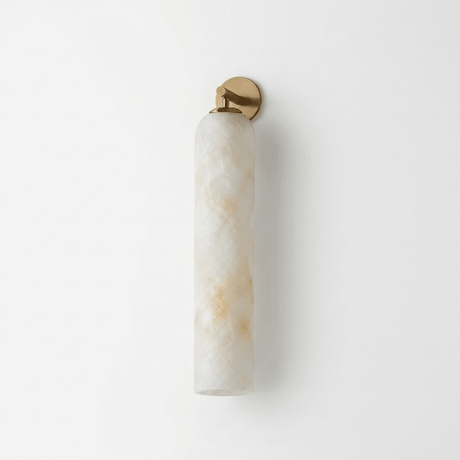 Tall carved stone tube wall light with a small gold cap on a pale wall