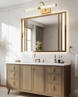 Brass arch and tube lit above a wide gilt mirror over a pale wood vanity