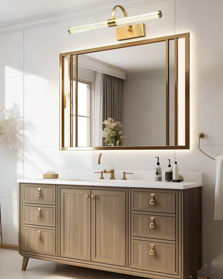 Brass arch and tube lit above a wide gilt mirror over a pale wood vanity