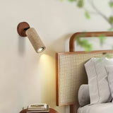 Travertine tube lit on a wall above a cane headboard and a side table