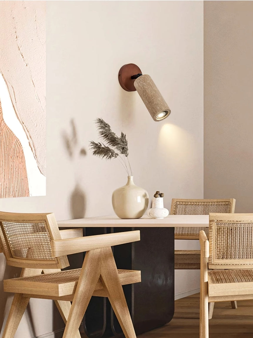Travertine tube lit on a plaster wall beside a dining table and chairs