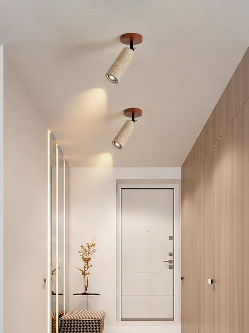 Two travertine tubes lit on a hallway ceiling above a pale wood floor