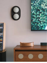 Black sconce on a pale wall above a wood console beside a green artwork