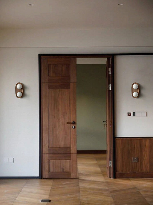 Two sconces lit either side of a wood doorway in a hallway with a floor